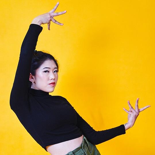 a woman in a black top holding her hands open in front of a yellow wall